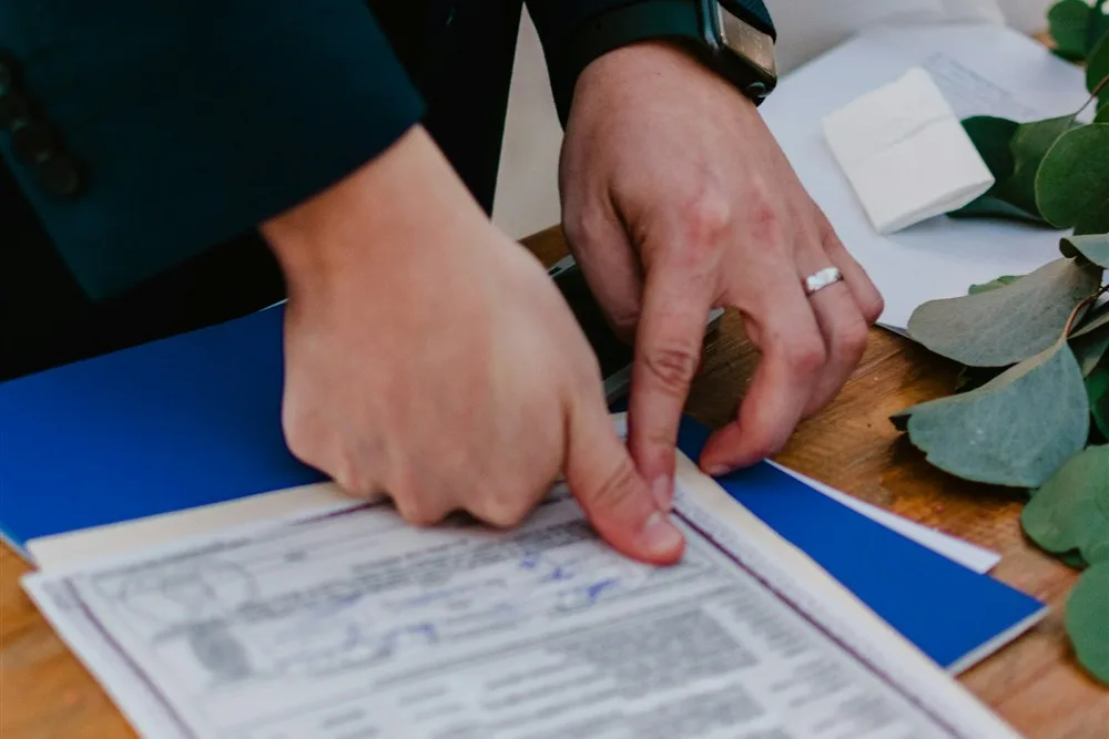 Mãos de noivos sobre a certidão de casamento durante a assinatura, sobre uma mesa de madeira