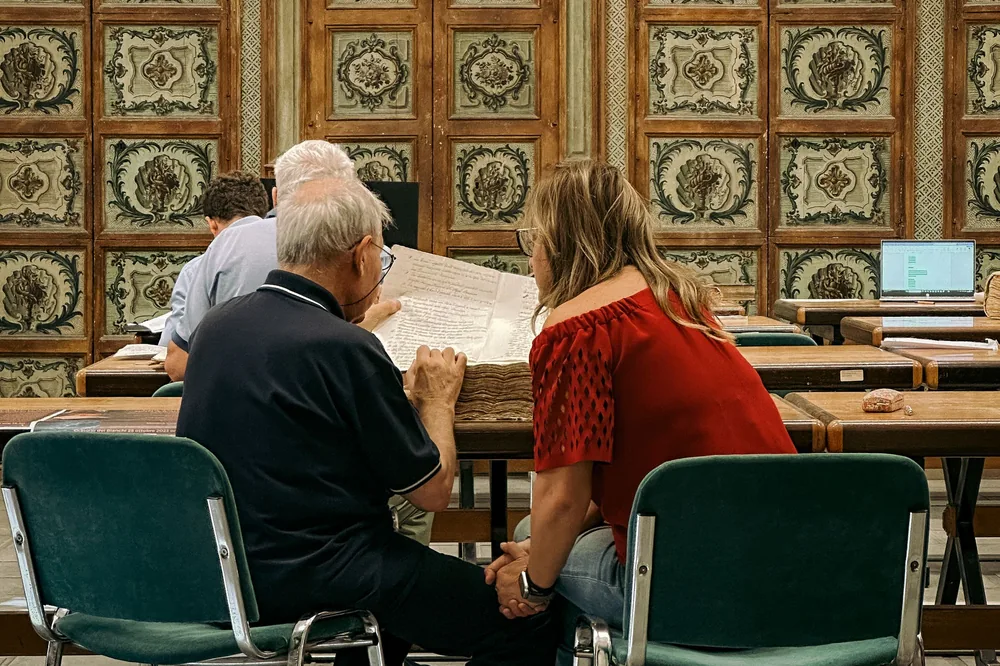 Duas pessoas consultando um documento antigo numa biblioteca histórica em Palermo, na Itália
