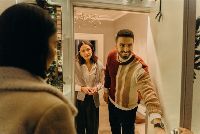 Casal recebe um visitante na porta de casa, cumprimentando quem chega