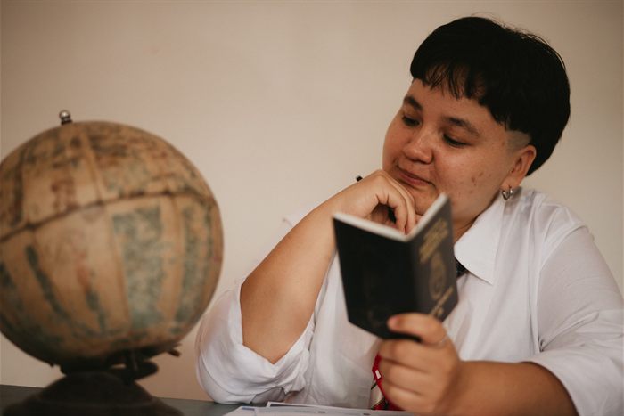 Jovem sentado lendo o próprio passaporte, com um globo ao lado, organizando a papelada do intercâmbio