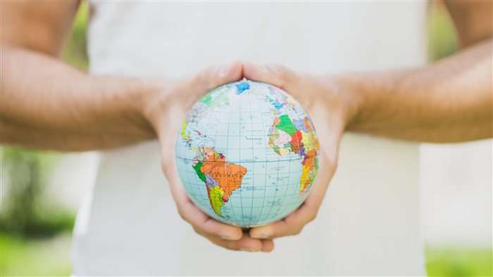 Mãos segurando um pequeno globo terrestre, representando a escolha de um destino para morar ou viajar