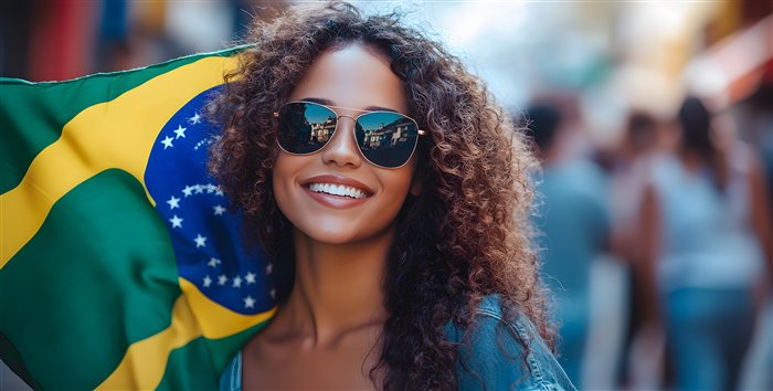 Mulher brasileira sorridente segurando a bandeira do Brasil em uma rua movimentada, representando brasileiros trabalhando no exterior