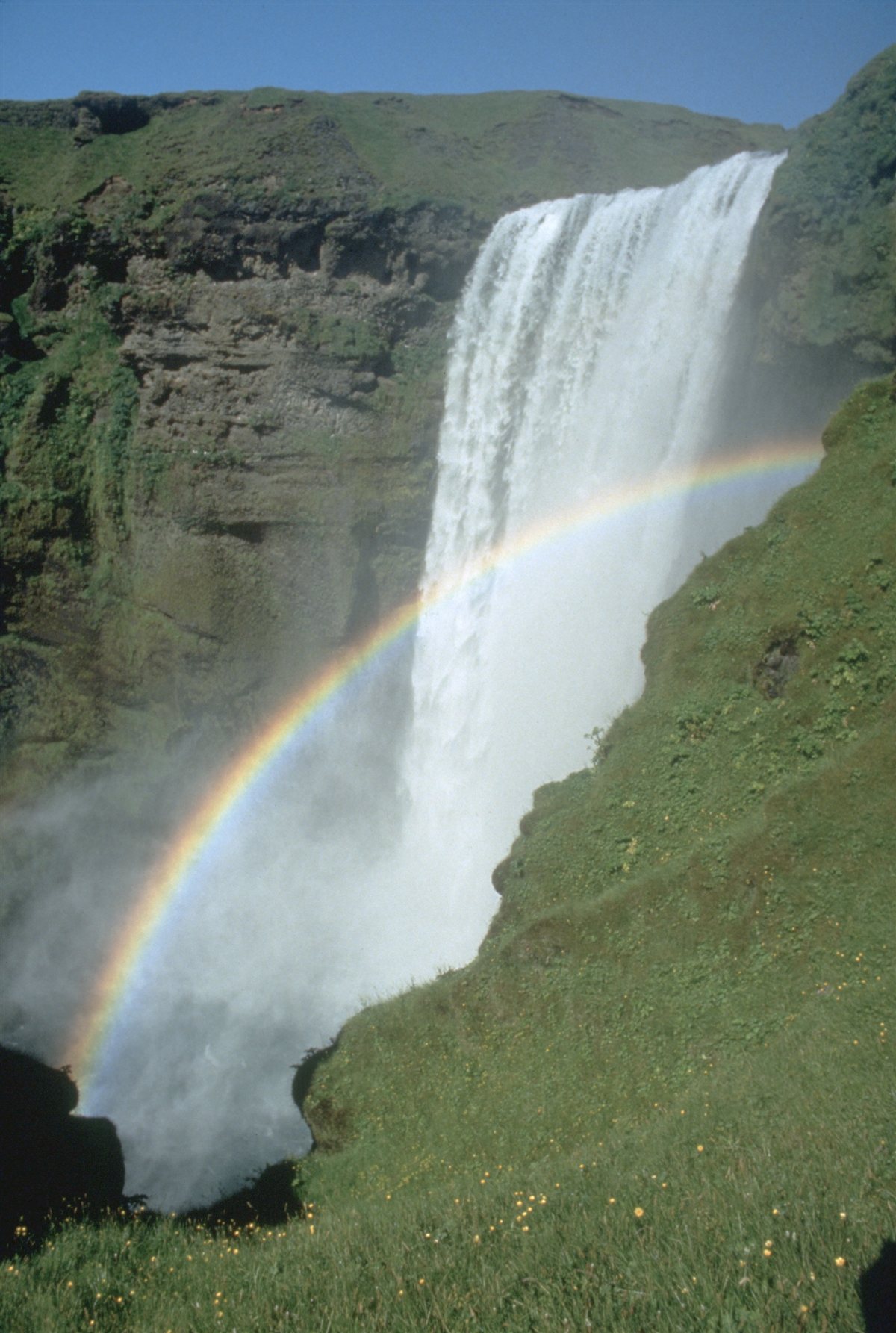 Cachoeira Skógafoss na Islândia, cercada por paisagem verde típica do país