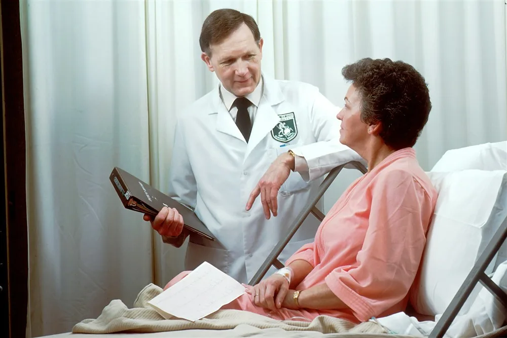 Médico de jaleco conversando com uma paciente em um quarto de hospital