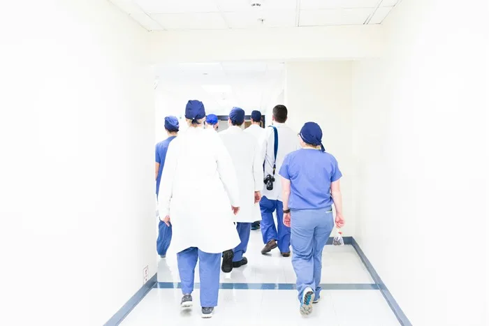 Equipe de profissionais de saúde de jaleco caminhando juntos por um corredor de hospital