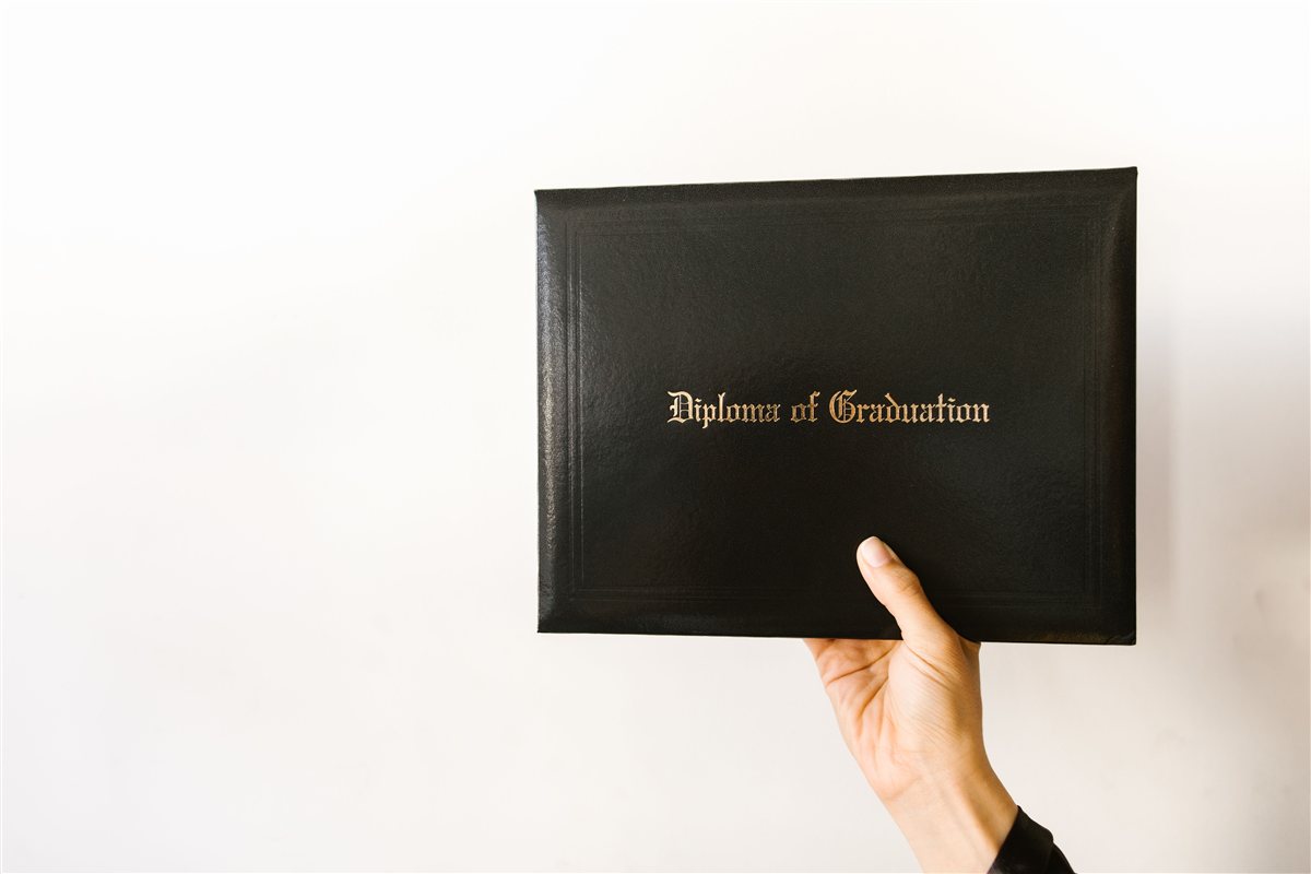Mão segurando uma pasta de diploma de graduação com capa preta e letras douradas
