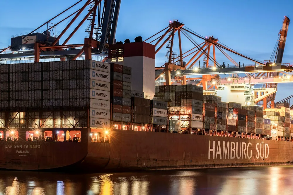 Navios cargueiros atracados no porto de Hamburgo, na Alemanha, ao anoitecer, com guindastes de contêineres iluminados