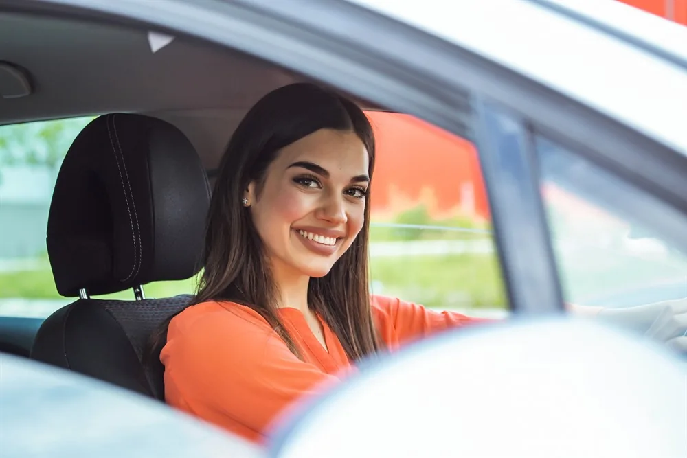 Mulher sorrindo ao volante de um carro, com o cinto de segurança afivelado