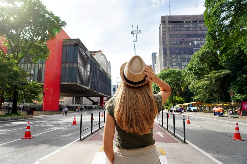 Mulher de chapéu, de costas, olhando a Avenida Paulista com o MASP ao fundo, em São Paulo